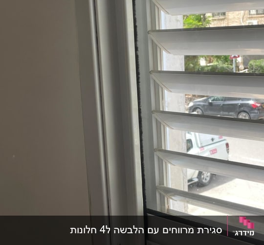 תריסים לבנים בחלון עם נוף חיצוני